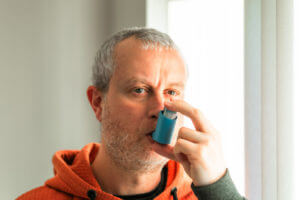 Man suffering from asthma using inhaler at home.