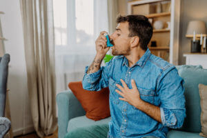 A young, asthma male patient uses an inhaler in his living room.